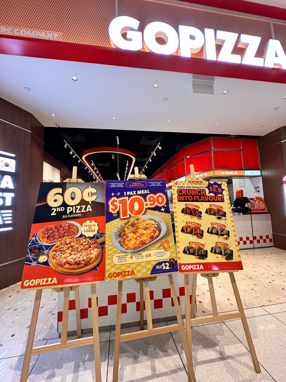 GoPizza Suntec City storefront with three concurrent promo standees — 60¢ 2nd Pizza, $10.90 1-Pax Meal, and $5.90 Crunch Into Flavour — May 2026