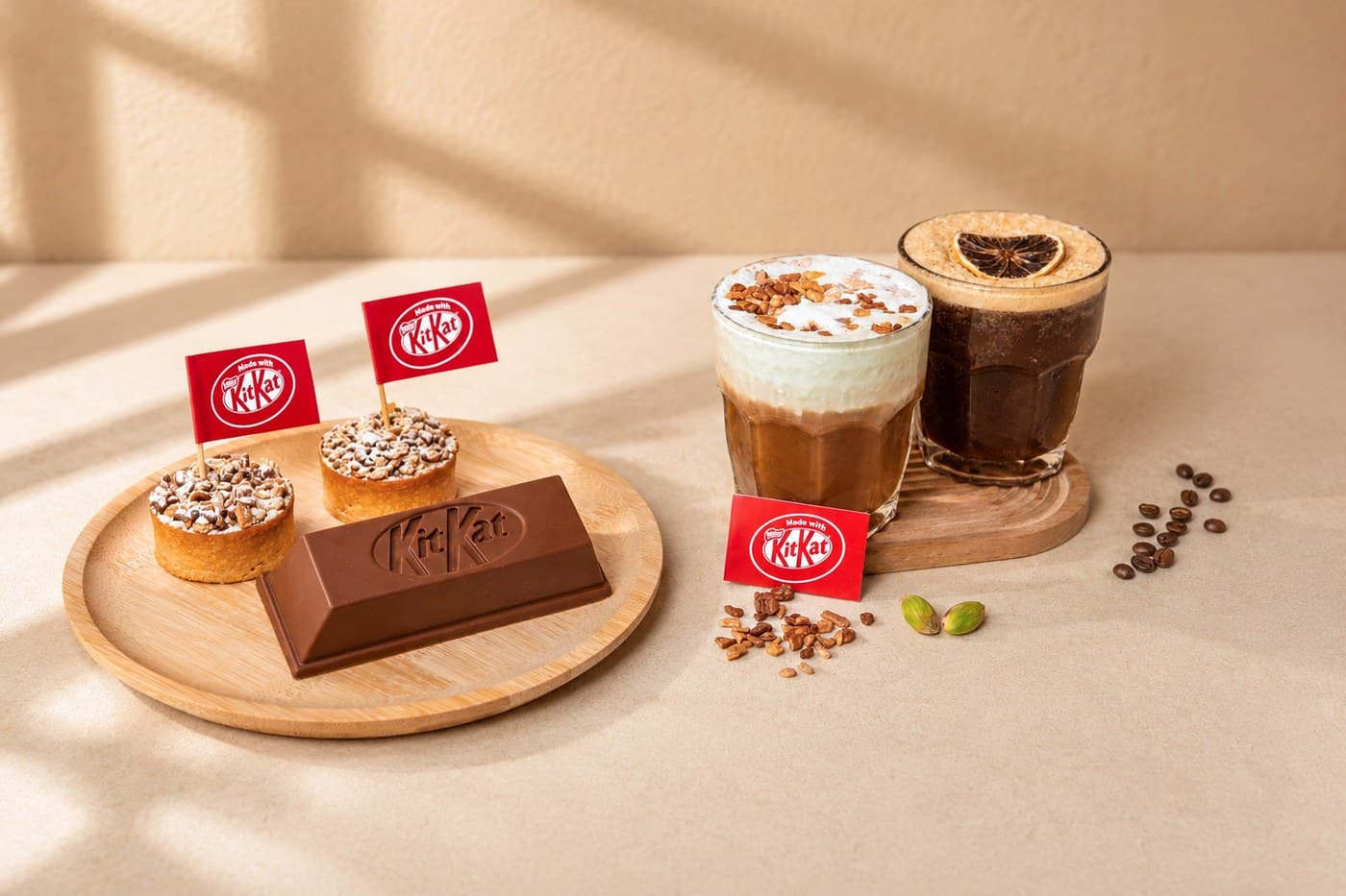 宜必思明古连 TASTE the Break 高茶的 KITKAT 甜点与迎宾饮品:木盘上两个 Made with KITKAT 挞与一块巧克力棒,旁边是 KITKAT 开心果摩卡与摇制柚子美式。