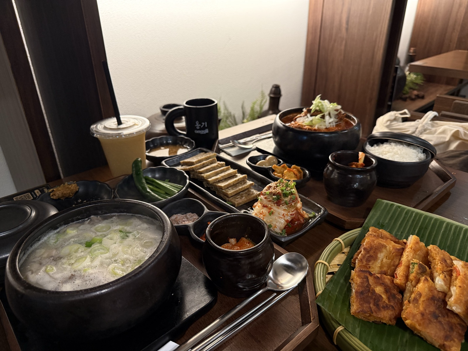 Onggii Novena Square 2 spread: milky beef gomtang, spicy beef stew, jeon platter on banana leaf, house kimchi and banchan.