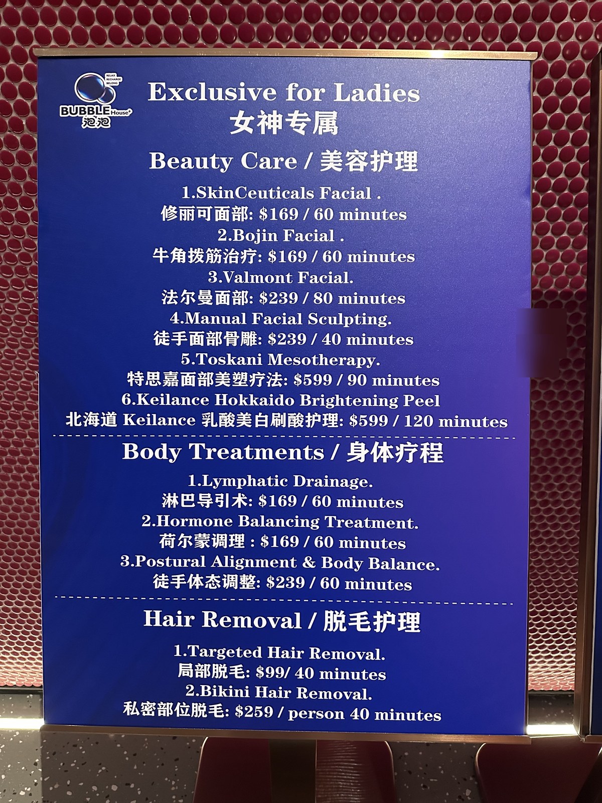 Pricing standee for "Exclusive for Ladies 女神专属" beauty care services at BUBBLE House. Three sections: Beauty Care (SkinCeuticals Facial $169/60min, Bojin Facial $169/60min, Valmont Facial $239/80min, Manual Facial Sculpting $239/40min, Toskani Mesotherapy $599/90min, Keilance Hokkaido Brightening Peel $599/120min). Body Treatments (Lymphatic Drainage $169/60min, Hormone Balancing $169/60min, Postural Alignment $239/60min). Hair Removal (Targeted $99/40min, Bikini $259/person 40min).