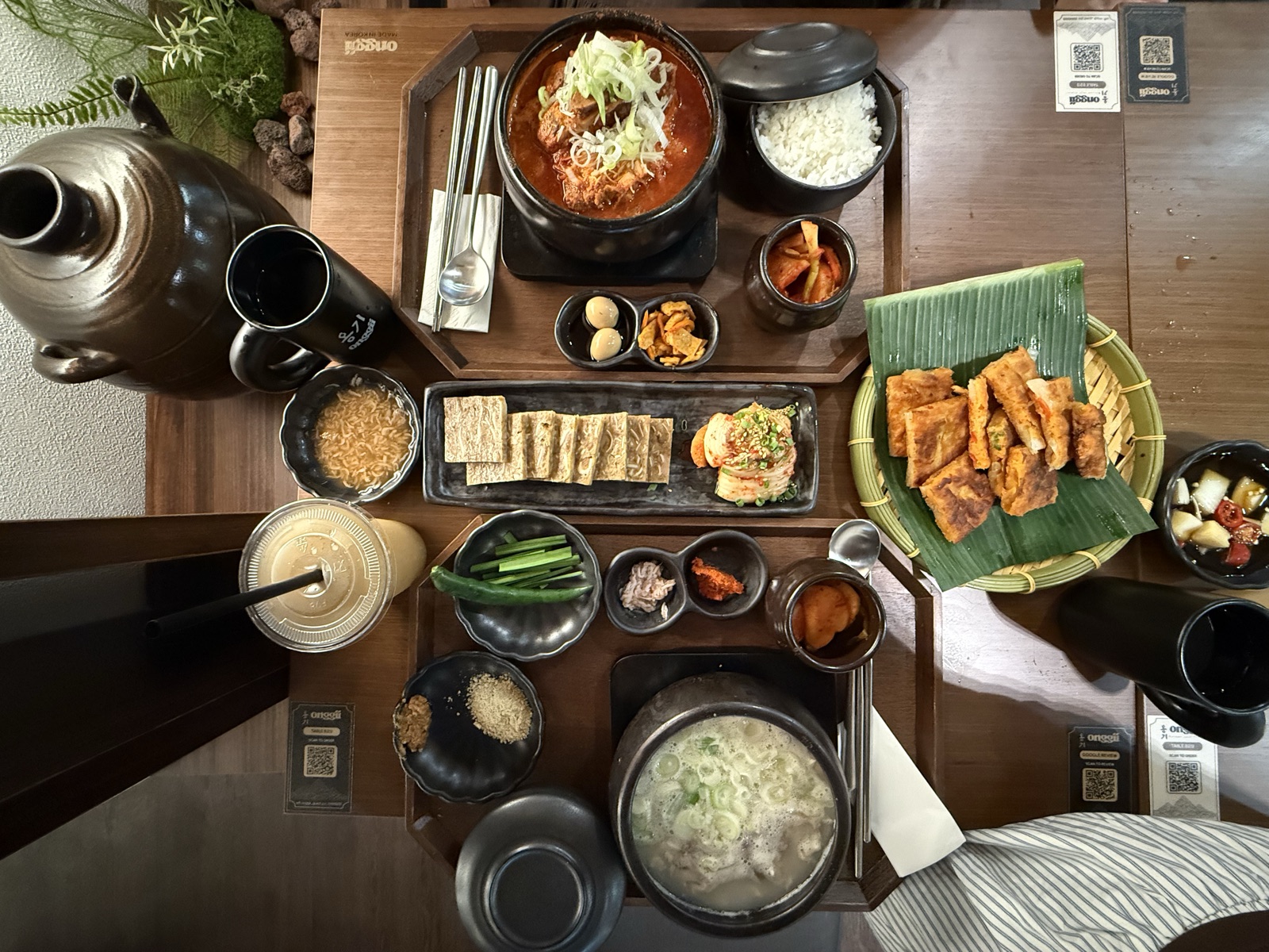 Top-down spread at Onggii: gomtang, spicy stew, jeon on banana leaf, banchan, rice in onggi bowls and yuja drink.