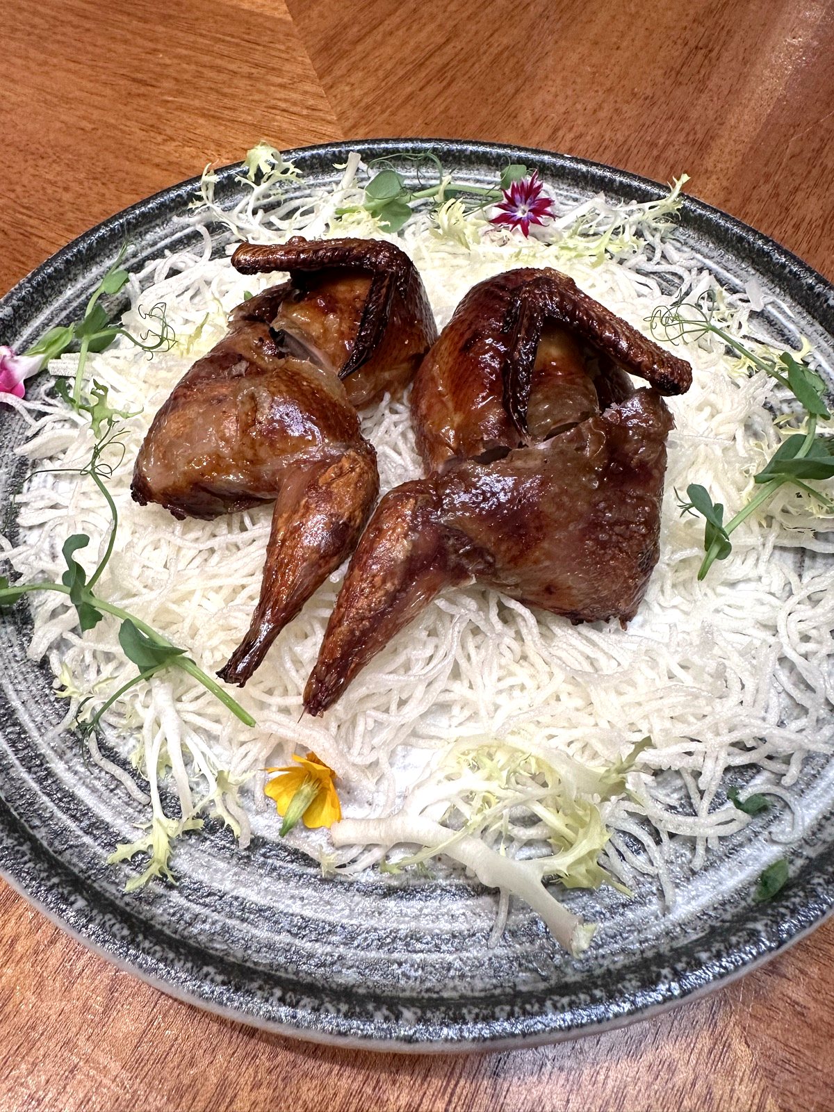 Crispy Deep-Fried Quail at Xin Cuisine, two burnished birds on a nest of crisped rice vermicelli with edible flowers.